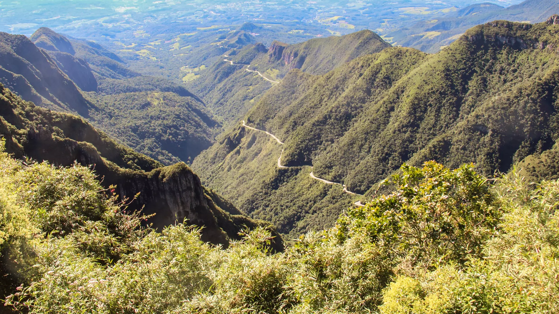 Estrada sinuosa cortando montanhas verdes, mostrando o Carnaval em ambiente de serra.